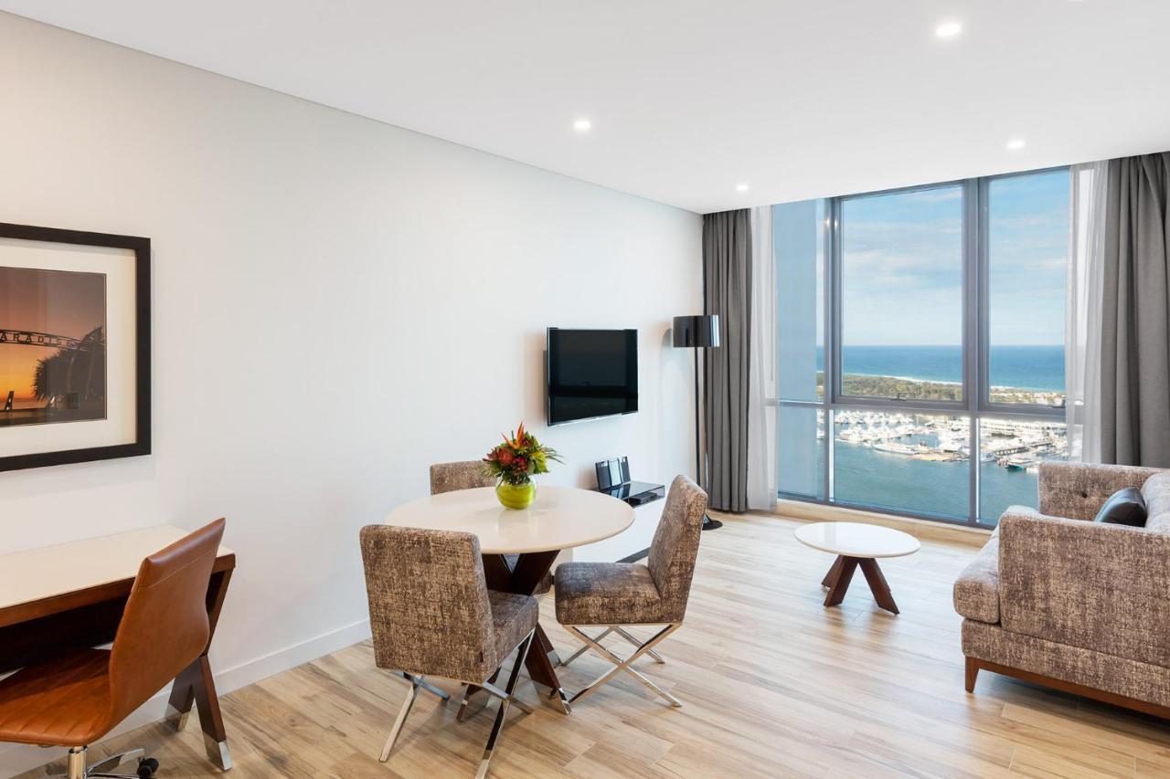 Meriton Suites Southport Gold Coast Buitenkant foto The photo depicts a modern living space, possibly a hotel suite or an apartment. It features a light-filled area with large windows offering a view of the water and a marina. 

Key elements include:

- A round dining table with chairs and a small vas
