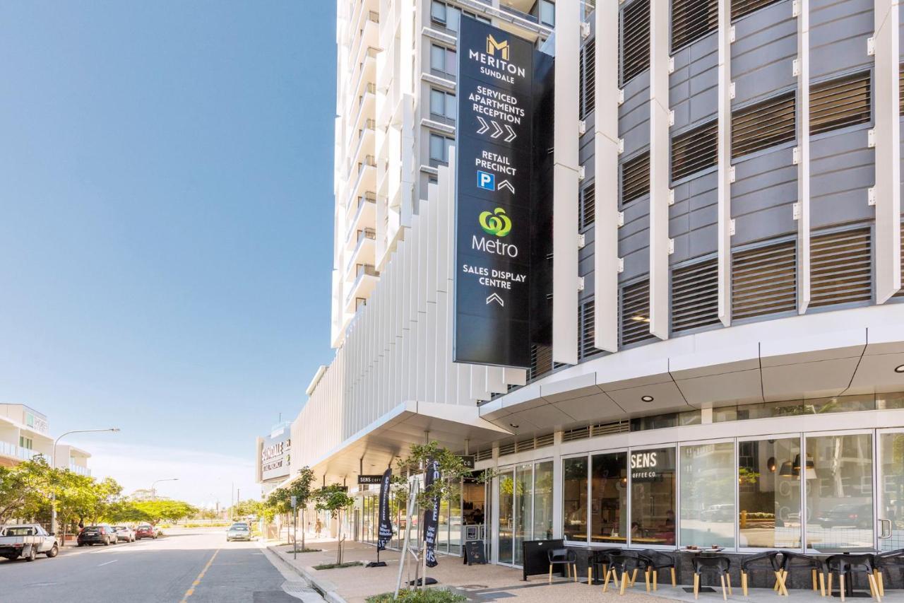 Meriton Suites Southport Gold Coast Buitenkant foto The photo shows a modern building with a sleek design, prominently featuring signage for a Hilton hotel. There are indications for amenities such as parking and a sales display center. The entrance appears to be spacious, flanked by trees and outdoor