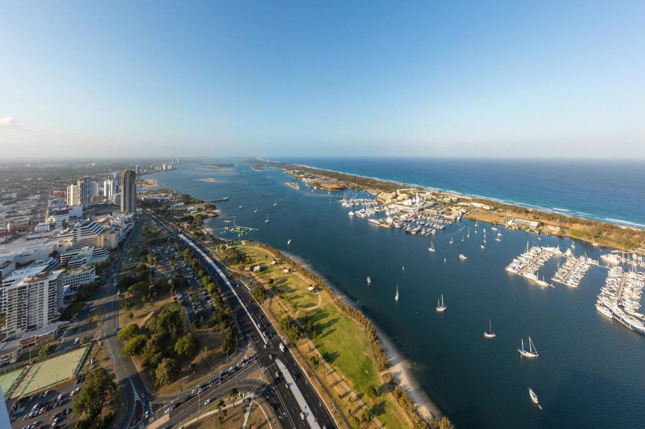 Meriton Suites Southport Gold Coast Buitenkant foto The photo depicts a scenic aerial view of a coastal area, featuring a wide river or inlet that flows into the ocean. Along the water, there are several boats anchored in a marina. On the land, there are green parks and well-maintained roads, along wi