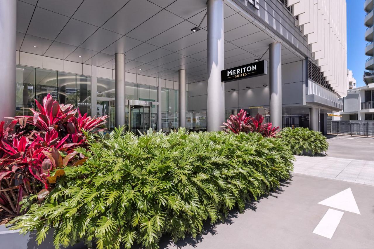 Meriton Suites Southport Gold Coast Buitenkant foto The photo shows the entrance of a building, specifically labeled "MERITON." It features a modern architectural design, with a glass facade and large columns. In front of the entrance, there are lush green plants, including ferns and colorful foliage,