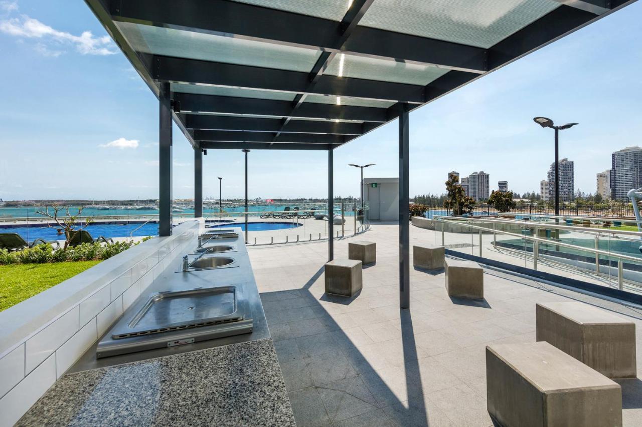 Meriton Suites Southport Gold Coast Buitenkant foto The photo shows a modern outdoor area featuring a shaded pavilion with a transparent roof. Underneath the structure, there are several sinks or wash stations made from stone or concrete. Nearby, there are minimalist concrete benches for seating. The 