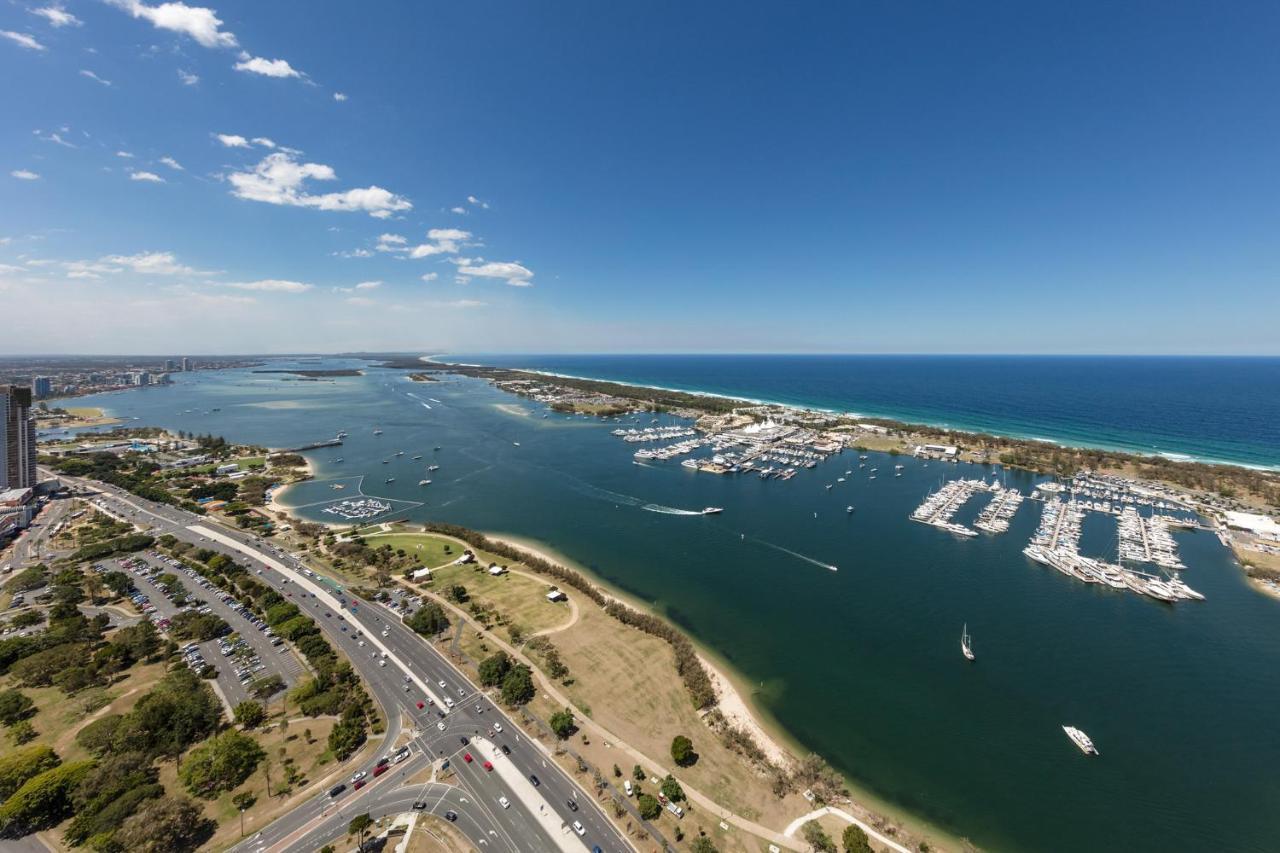 Meriton Suites Southport Gold Coast Buitenkant foto The photo shows a scenic coastal view featuring a river or inlet that flows into the ocean. On one side, there are several boats docked in a marina, indicating a vibrant boating scene. The water appears calm, with some small boats seen moving through